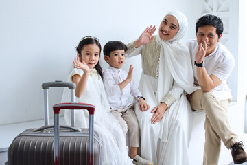 Happy Asian muslim family waving hands together ready to go mudik during Eid Mubarak moment.
