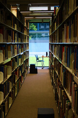 A typical library study desk and chair seen at the far end of two towering shelves of books