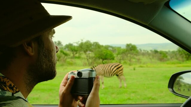 A male tourist wearing a safari hat takes pictures of animals in a savannah in Africa. a male traveler sits in a safari vehicle and takes a photo of wild animals in a national reserve zebra