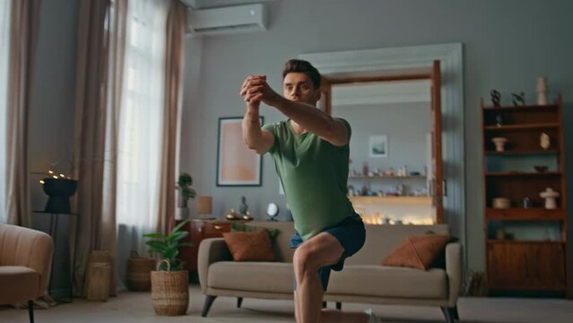 Active sportsman making squats in living room. Focused young man training body