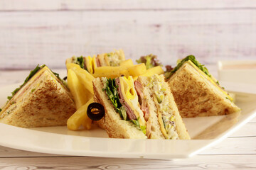 CLUB SANDWICH with olive and french fries served in dish isolated on table closeup side view of fastfood