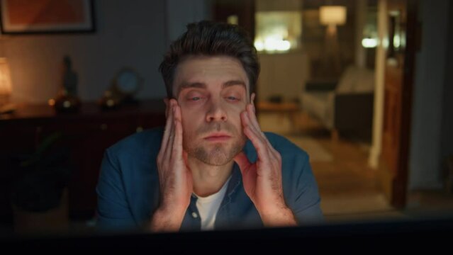 Exhausted man rubbing temples working at night flat closeup. Tired freelancer