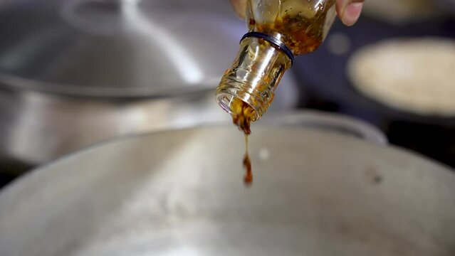 Chef pours chilli garlic sauce flavours into spicy Indian cuisine SLOW MOTION, CLOSE-UP