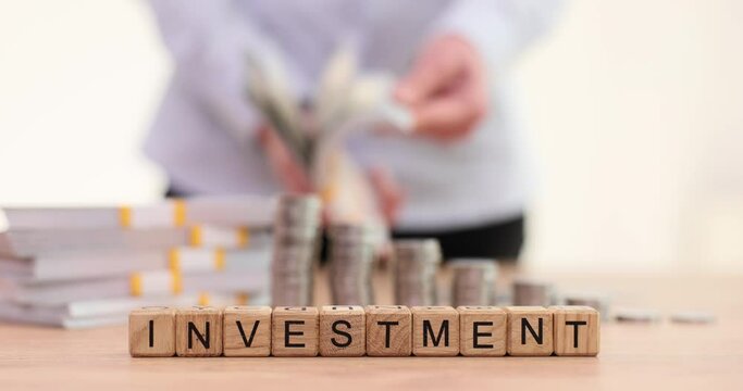 Wooden blocks with word investment in background woman is counting wad of money