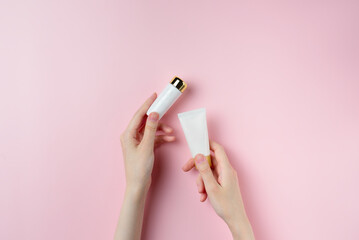A woman's hand holds two white tubes on a pastel pink background