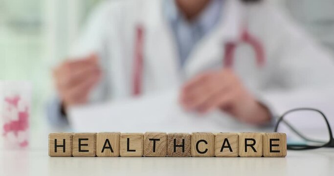 Wooden blocks with inscription healthcare on background of doctor