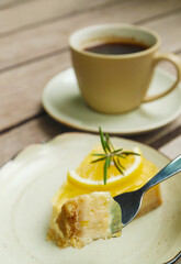 Fork scooping mouthwatering lemon cream cheese pie with blurry coffee cup in the backdrop