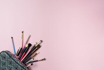 Makeup brushes falling out of cosmetics on pink background