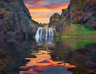 Stjornarfoss waterfall reflected in the calm waters of small river. Dramatic summer sunrise in...