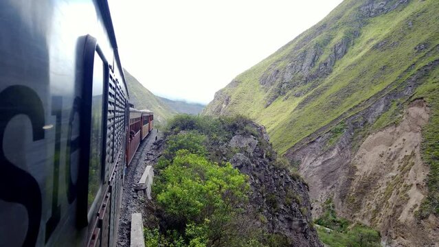 Train journey through the lush green Alausi mountains of Ecuador, cloudy skies overhead, dynamic side view