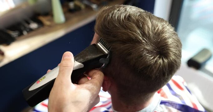 Hairdresser cuts young man hair with hair clipper