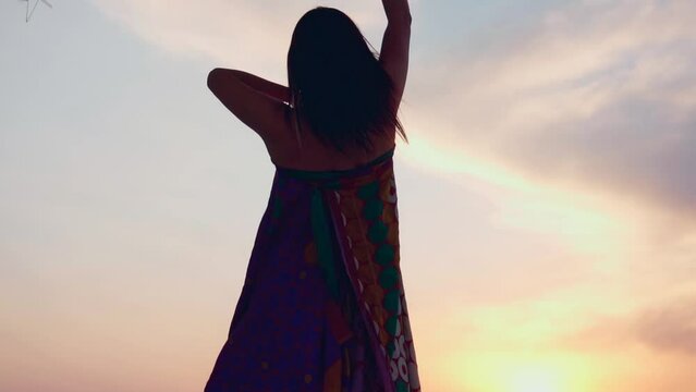 Young dancer stands on the top of a mountain at sunset, performing an emotional and fluid dance. Concept: freedom, passion and connection with nature.