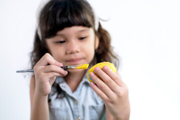 Little girl paints Easter eggs on white background, selective focus