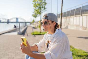 Young Hispanic hipster girl browsing mobile phone while sitting in street with takeaway beverage. 