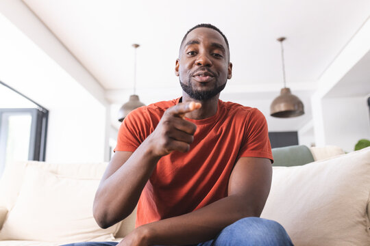 African American man in a red shirt is holding a remote and relaxing on a couch on video call