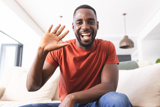 African American man in a red shirt waves with a bright smile on video call