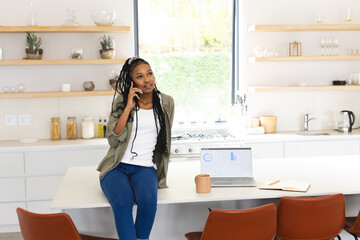 A young African American woman chats on the phone, leaning on a kitchen island with copy space
