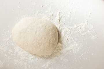 A ball of dough sits amidst a dusting of flour on a surface with copy space