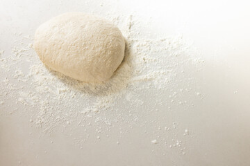 A ball of dough sits atop a dusting of flour on a white surface with copy space