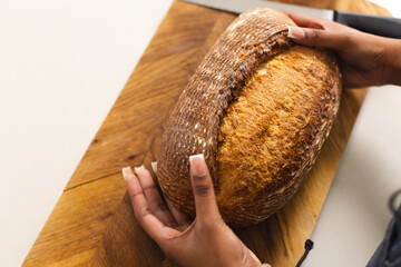 Hands slice a large loaf of bread on a wooden cutting board with copy space