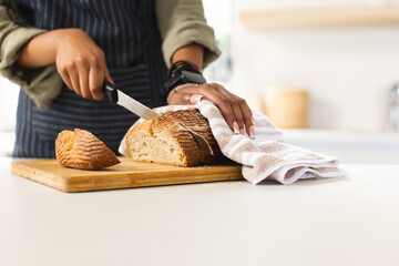 Person slices a loaf of bread on a wooden cutting board in a bright kitchen with copy space