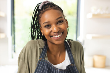 A young African American woman smiles warmly, wearing a striped apron