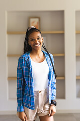A young African American woman smiles brightly, wearing a blue plaid shirt and white top