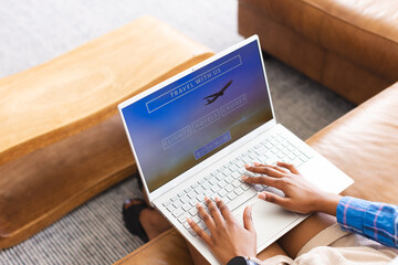 A person is booking travel online, fingers poised over a laptop keyboard