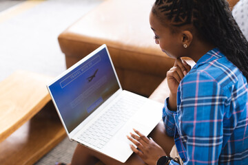 A young African American woman focuses on her laptop screen, booking a vacation online