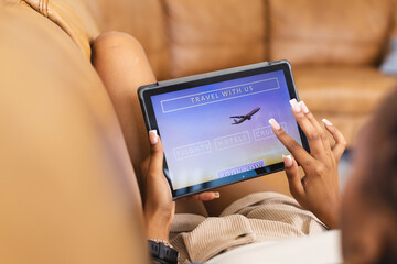 A young African American woman browses travel options on a tablet, booking a vacation online