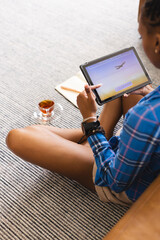 Young African American woman is using tablet while sitting on floor to book vacation online © wavebreak3