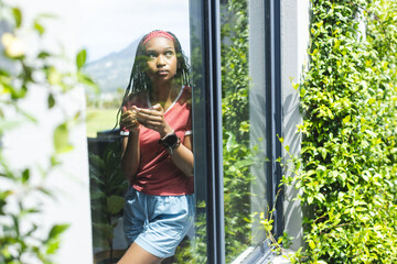 A young African American woman gazes thoughtfully through a window with copy space