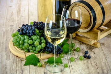 The image depicts a cluster of ripe grapes juxtaposed with a glass of deep-red wine. The grapes, with their vibrant hues of purple and green, exude freshness and abundance. Meanwhile, the wine in the 