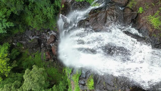 Water from a rainforest stream rushes over a sheer rock cliff creating a spectacular waterfall. Static drone view