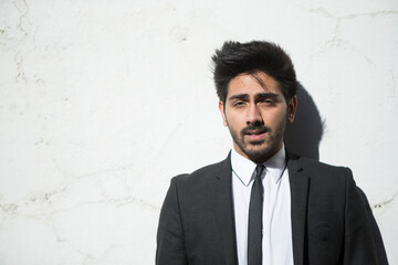 Indian businessman leaning against a stone wall.