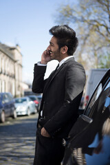 Indian businessman leaning against  his car and talking on phone.