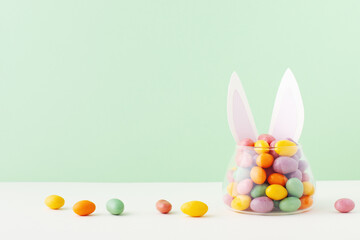 Colorful candy jar decorated with bunny ears against green background, gifts for Easter
