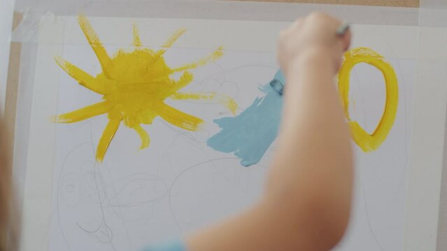 Close-up of a child's hand painting a colorful sun and sky on canvas. Early childhood art and creativity development concept. Design for educational program brochures, child development articles, and