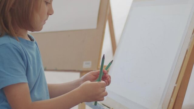 Child holding pencils in front of a canvas with a sketch, preparing to paint. Early art education and creative development concept. Design for art class advertisements, educational content, and