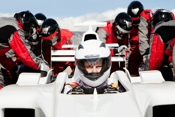 Racing team prepping a racecar with focused driver ready at the wheel. 