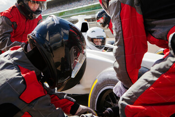 Racecar driver focused before the start surrounded by pit crew. 