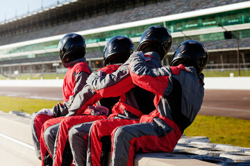 A team of racing drivers in matching red suits taking a break at the racetrack. 