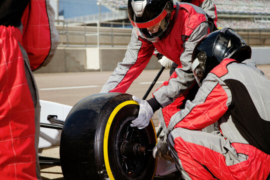 Pit crew in red suits changing a tire during a race. 