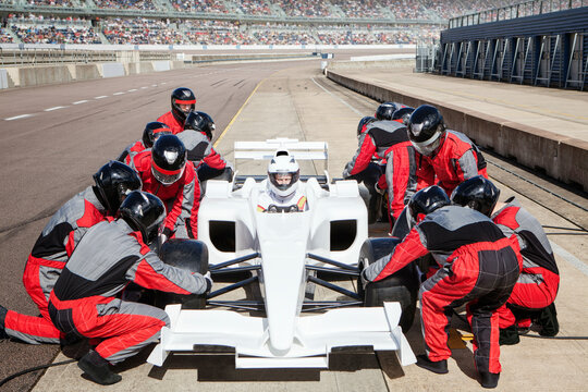 Pit crew in red uniforms servicing a white race car on the track. 