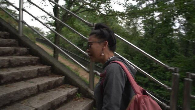 As an Asian woman ascends the 398 steps, she proudly displays her postcard featuring the Chureito Pagoda, eager to reach the hilltop overlooking Mt. Fuji at Arukarayama Sengen Park in Japan.