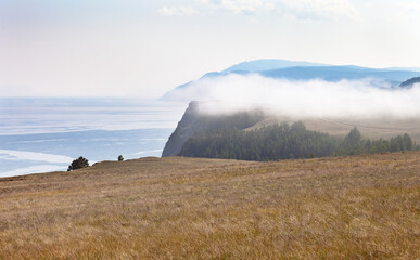 Baikal Lake in August. Cold fogs hang over the coastal cliffs near Shunte Left on the shore of Olkhon Island