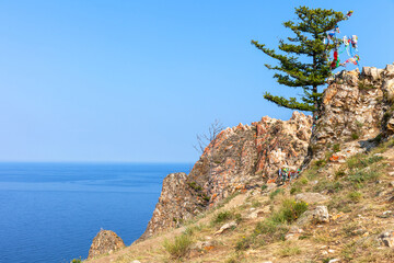 Baikal Lake in summer sunny day. View of larch tree with colorful tourists ribbons on rocky Cape Shunte Left or as it is also called Cape of Love on Olkhon Island. Beautiful summer landscape