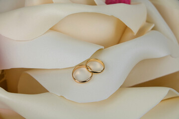 Two gold wedding rings lie on the petal of a light yellow artificial rose