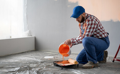 House painter pouring orange wall paint into tray, preparing for renovation and remodeling...