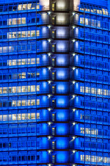 Blau illuminierte Fassade eines Bürohochhaues bei Nacht in der Dunkelheit mit teilweise beleuchteten Großraumbüros